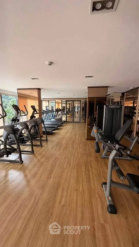 Spacious gym with modern fitness equipment and wooden flooring in a residential building.