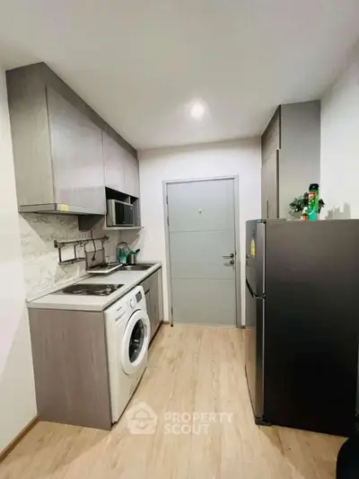 Modern compact kitchen with washing machine and fridge in sleek apartment.