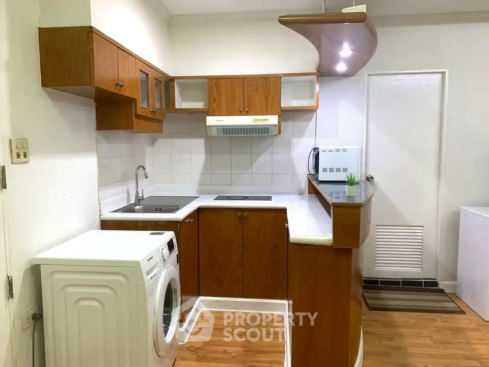 Charming kitchen with wooden cabinets and modern appliances, featuring a washing machine and sleek countertop.