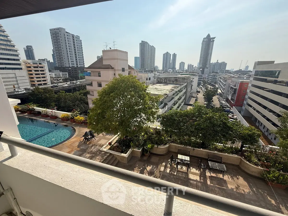 Stunning cityscape view from a balcony overlooking a pool and lush greenery, perfect for urban living.