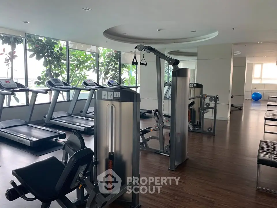 Spacious gym with modern equipment and large windows offering natural light.