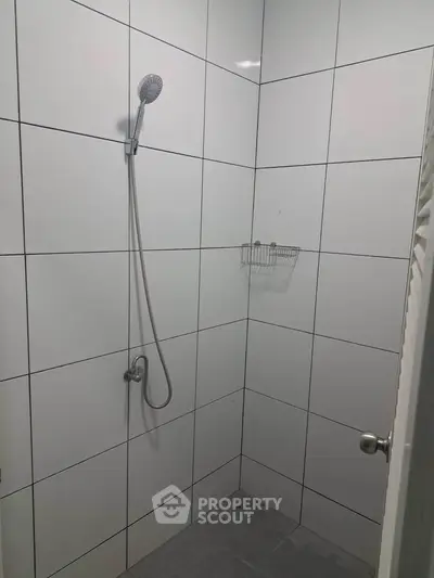 Minimalist bathroom shower area with white tiled walls and modern fixtures.