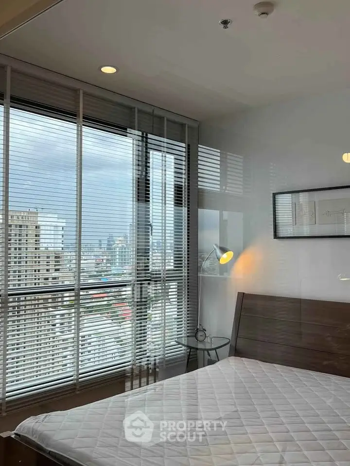 Modern bedroom with city view and large windows in high-rise apartment.