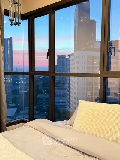 Luxurious bedroom with stunning city view through large windows at sunset.