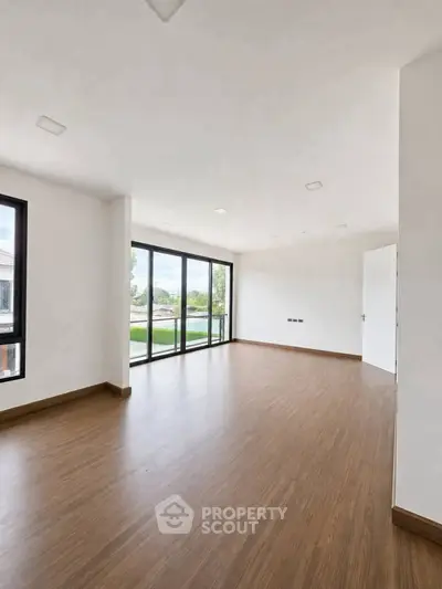 Spacious empty living room with large windows and wooden flooring, offering a bright and airy atmosphere.