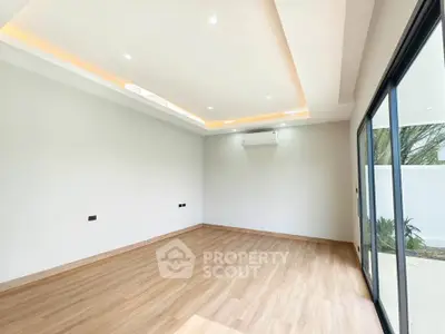 Spacious modern living room with wooden flooring and large sliding glass doors opening to a garden view.