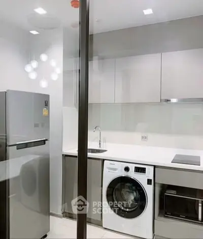 Modern kitchen with sleek appliances including fridge, washing machine, and microwave in a compact layout.