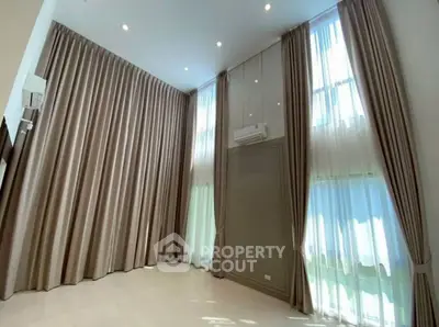 Spacious living room with high ceilings and elegant floor-to-ceiling curtains.