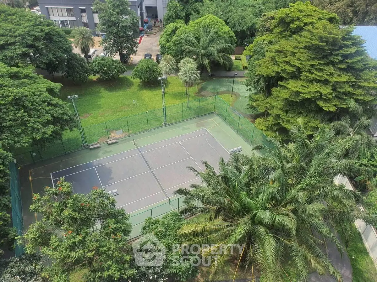 Lush green tennis court surrounded by trees in a serene residential complex.