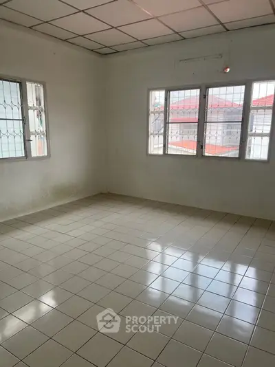 Spacious empty room with tiled flooring and large windows, perfect for customization.