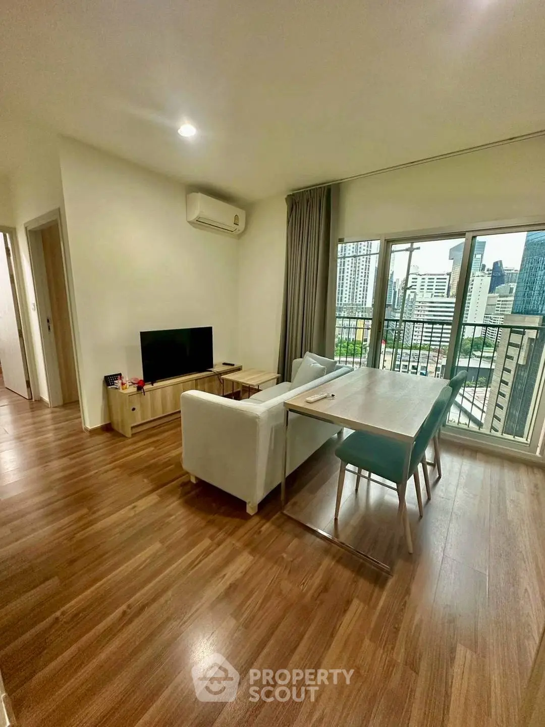 Modern living room with city view, featuring sleek furniture and wooden flooring.