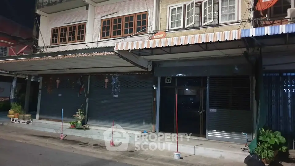 Street view of commercial buildings with closed shutters at night, showcasing potential retail space.