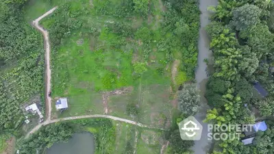 Aerial view of lush green land with river and pathways, ideal for development.