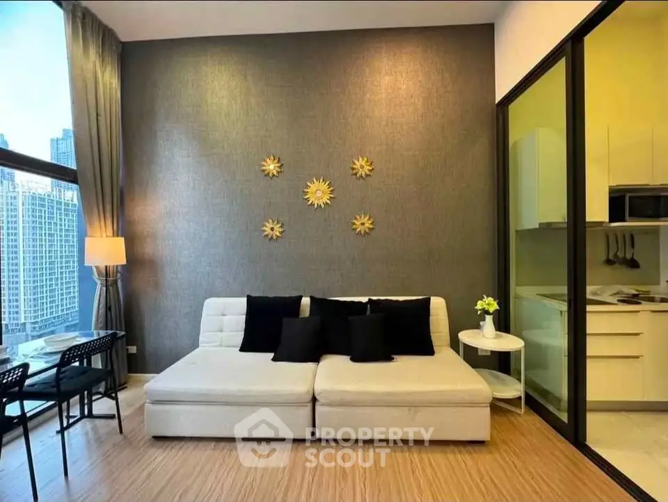 Modern living room with stylish decor and adjacent kitchen in a high-rise apartment with city view.