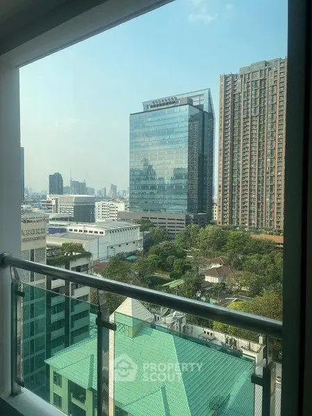 Stunning cityscape view from high-rise balcony overlooking modern buildings and lush greenery.
