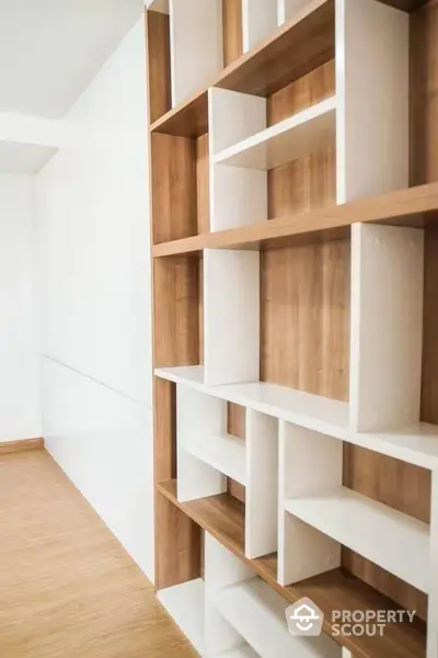 Spacious and modern living area with custom-built wooden shelving unit, perfect for displaying decor or organizing books, complemented by pristine white walls and warm wooden flooring.