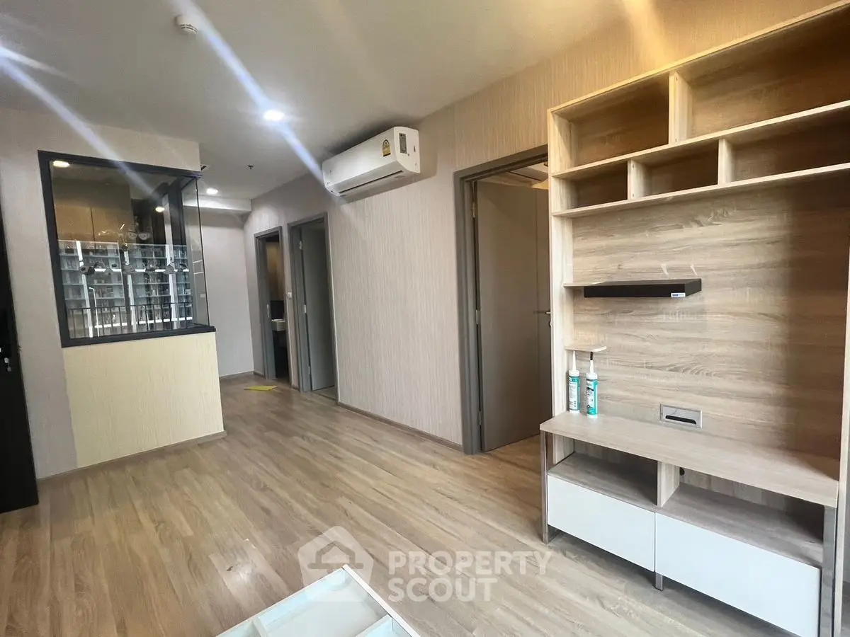 Modern living room with wooden flooring and built-in shelves, featuring air conditioning and sleek design.