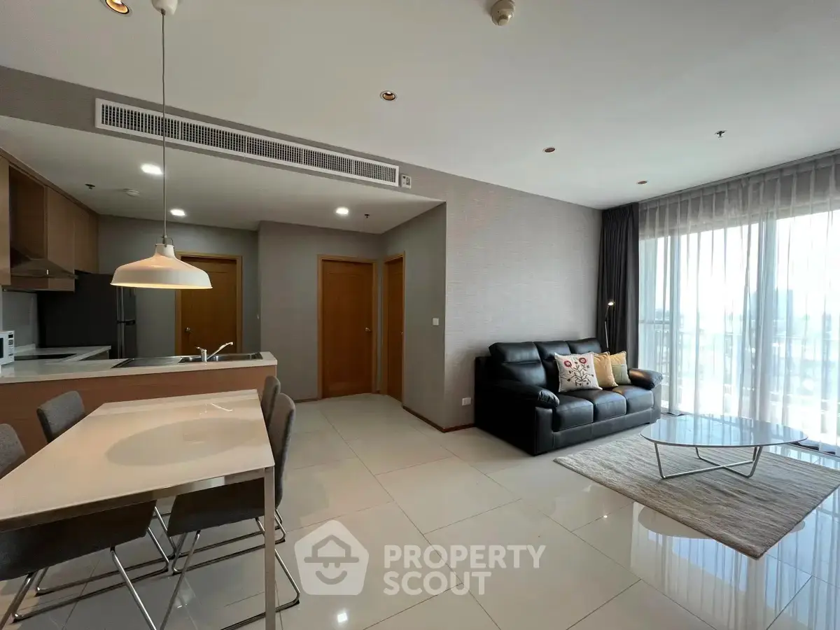 Modern open-plan living room with sleek kitchen and city view, featuring stylish furniture and ample natural light.