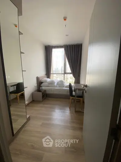 Cozy bedroom with modern furnishings and large window offering natural light and city views.
