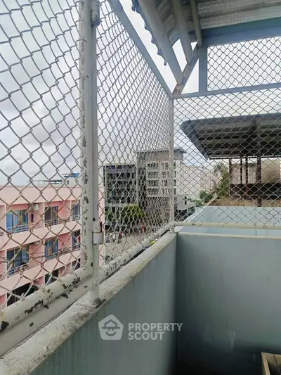 Urban balcony view with chain-link fence and cityscape backdrop