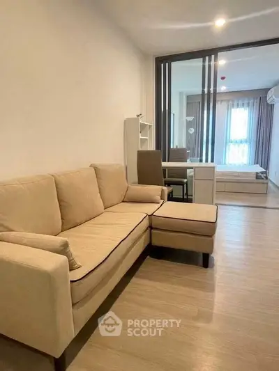 Modern living room with beige sofa and open layout leading to bedroom.