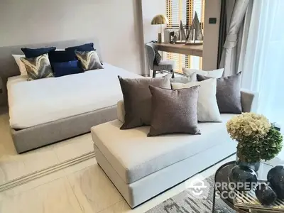 Elegant living room with plush neutral-toned sofas, accented by navy blue pillows, complemented by a chic glass coffee table and decorative shelving.