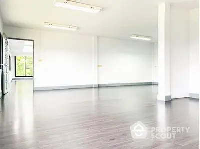 Spacious and bright empty room with polished wooden flooring, large windows allowing ample natural light, and a clean, modern aesthetic.