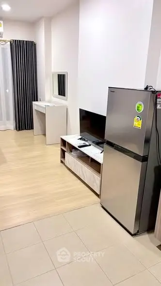 Modern apartment interior with fridge and TV in open living space.