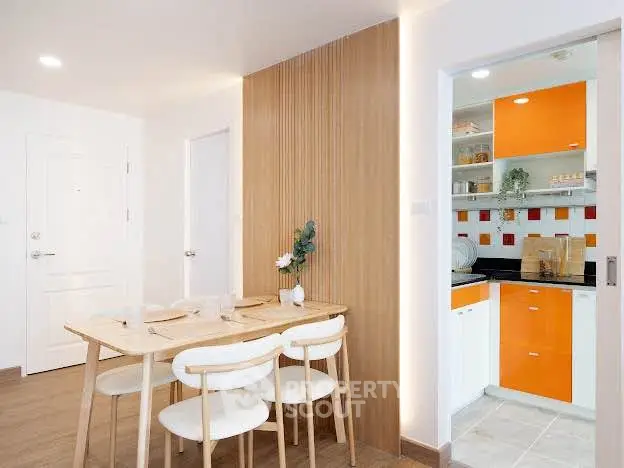 Modern dining area with wooden accents and view into vibrant orange kitchen.