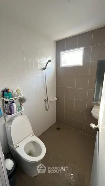 Modern bathroom with sleek shower and toilet, featuring neutral tiles and natural light.