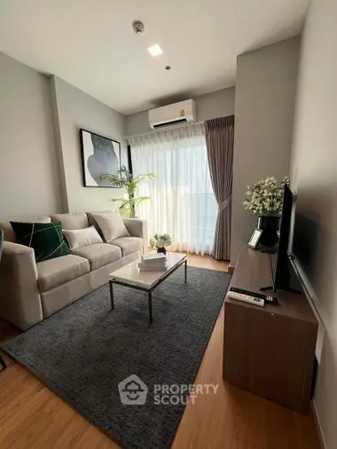 Elegant living room with plush sofa set, modern entertainment unit, and large windows draped in sheer curtains, accentuated by tasteful decor.