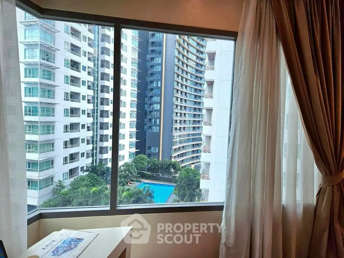 Stunning cityscape view from a high-rise apartment window overlooking a pool and modern buildings.