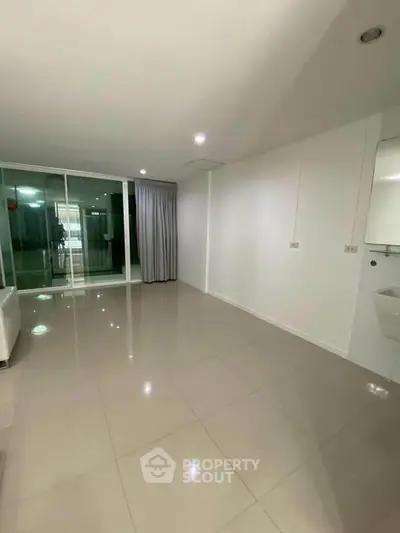 Spacious empty living room with glossy tiled floors and large windows for natural light.
