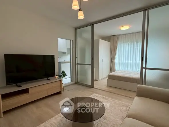 Modern living room with TV and glass partition leading to a cozy bedroom.