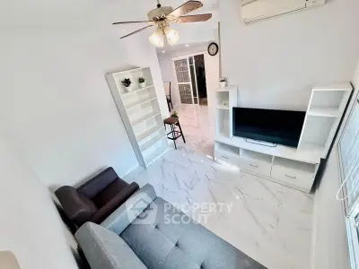 Modern living room with sleek furniture and marble flooring, featuring a ceiling fan and natural light.