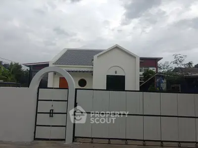 Charming modern house with unique architecture and gated entrance under cloudy sky.