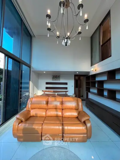 Spacious living room with high ceilings and elegant chandelier, featuring a cozy leather sofa and modern shelving.