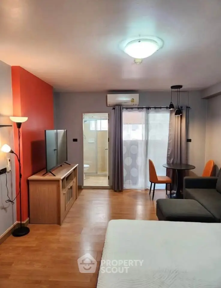 Modern studio apartment with open layout, featuring a cozy living area, dining space, and visible bathroom entrance.