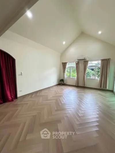 Spacious living room with high ceiling and large windows, featuring elegant herringbone wood flooring.