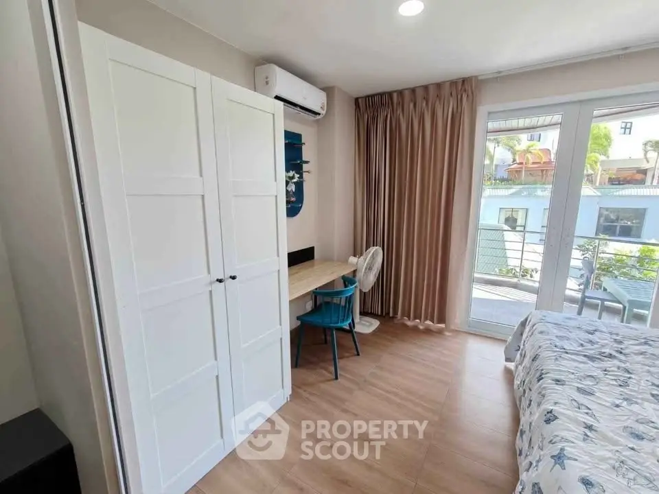 Bright bedroom with balcony access, featuring a wardrobe, desk, and air conditioning.