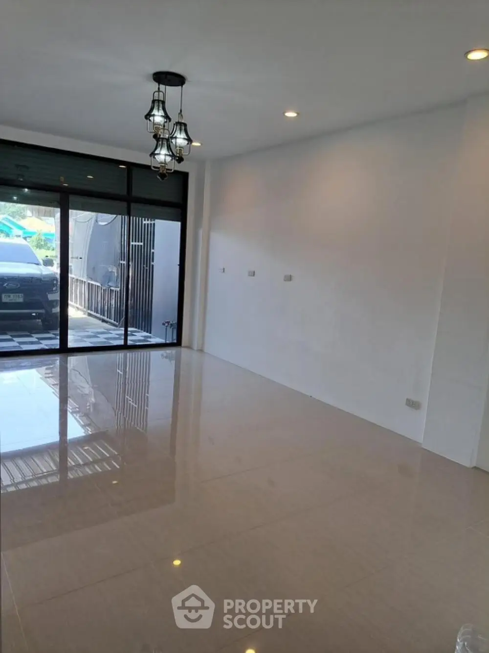 Spacious and bright living area with glossy tiled floors, elegant chandelier lighting, and large sliding glass doors leading to an outdoor view, perfect for modern living.