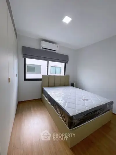 Modern bedroom with large window and air conditioning, featuring a comfortable bed and ample closet space.