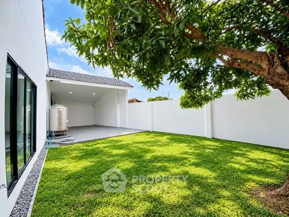 Spacious backyard with lush green lawn and tree, adjacent to modern home exterior.