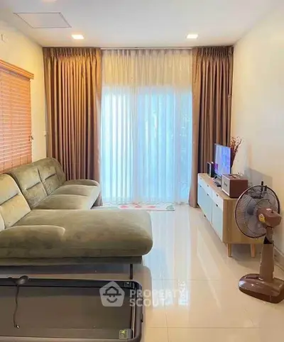 Modern living room with stylish sofa, TV unit, and floor fan, featuring elegant curtains and bright flooring.