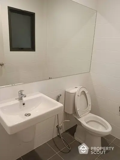 Pristine white bathroom with modern fixtures, including a wall-mounted sink, toilet, and a sleek mirror, offering a clean and minimalistic design.