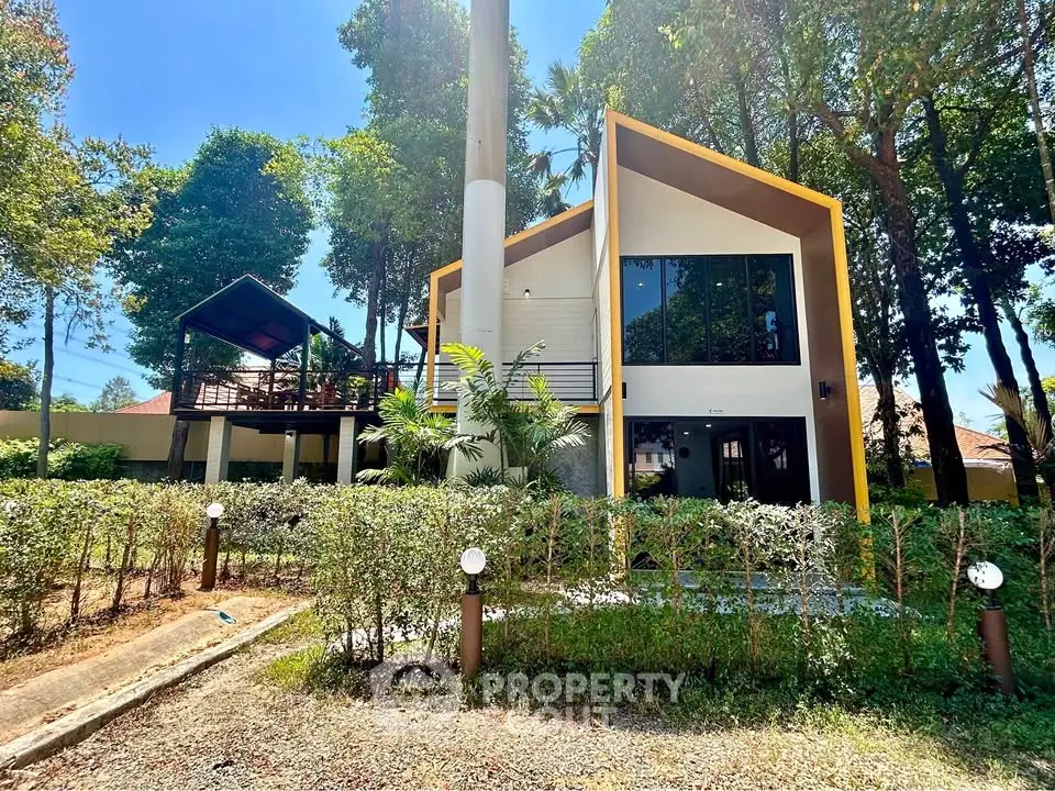 Modern architectural house with large windows surrounded by lush greenery and trees, offering serene living environment.