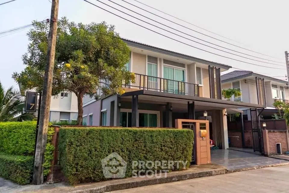 Modern two-story house with spacious balcony and lush greenery in a serene neighborhood.
