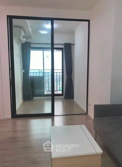 Modern living room with sliding glass doors leading to a balcony, featuring sleek furniture and natural light.