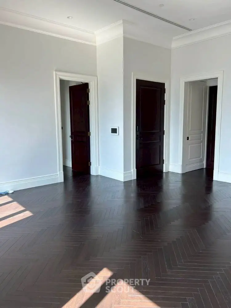 Elegant room with dark herringbone wood flooring and white walls, featuring multiple doors.