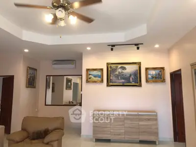 Spacious living room with elegant decor and ceiling fan, featuring framed artwork and comfortable seating.